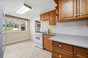 Kitchen featuring white appliances, wood finish cabinetry, light floors, light countertops, and decorative backsplash