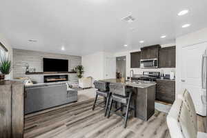 Kitchen with dark wood finish cabinets, open floor plan, light stone countertops, an island with sink, and a kitchen breakfast bar