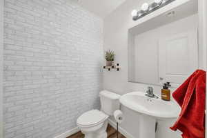 Half bathroom with wood finished floors and brick wall