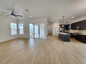 Kitchen with open floor plan, stainless steel appliances, a center island with sink, and light wood-type flooring