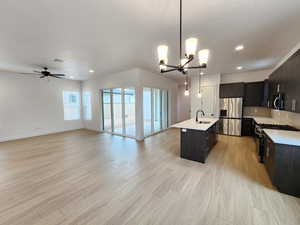 Kitchen with open floor plan, stainless steel appliances, suspended lighting, an island with sink, and light wood-type flooring