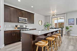 Kitchen with stainless steel appliances, dark wood finish cabinets, light wood finished floors, and a kitchen island with sink