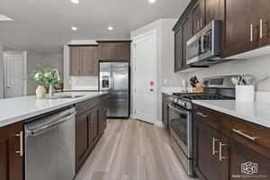Kitchen featuring stainless steel appliances, dark wood finish cabinets, light wood-type flooring, light stone counters, and recessed lighting