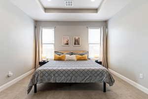 Bedroom with a tray ceiling, light carpet, and recessed lighting
