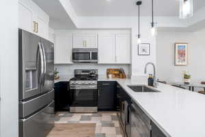 Dual tone kitchen with two tone cabinets, stainless steel appliances, light stone countertops, a peninsula, and pendant lighting