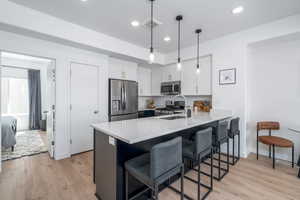 Dual tone kitchen featuring stainless steel appliances, a kitchen breakfast bar, a peninsula, light wood-style floors, and two tone cabinetry