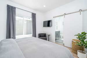 Bedroom featuring a barn door, light wood-style flooring, connected bathroom, and recessed lighting