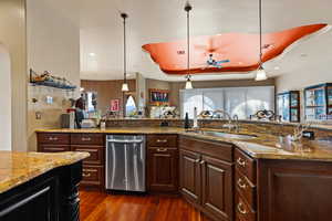 Kitchen featuring dark stone countertops, pendant lighting, dishwasher, a ceiling fan, and a raised ceiling