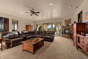 Living room with light carpet, a stone fireplace, ceiling fan, and recessed lighting