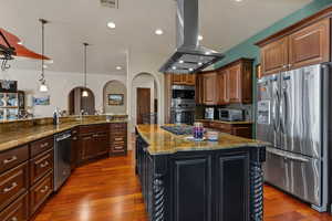 Kitchen with stainless steel appliances, island range hood, hanging light fixtures, arched walkways, and dark stone counters
