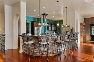 Kitchen with arched walkways, a kitchen bar, stainless steel refrigerator with ice dispenser, island exhaust hood, and hanging light fixtures