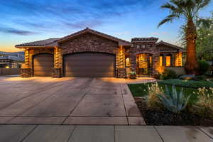 View of front of house featuring stone siding, a garage, concrete driveway, a tiled roof, and a gate
