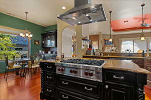 Two tone kitchen featuring island exhaust hood, dark stone counters, stainless steel gas stovetop, a chandelier, and dual tone cabinetry