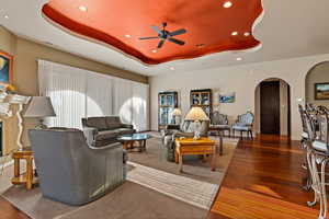 Living room with arched walkways, a ceiling fan, wood-type flooring, recessed lighting, and a raised ceiling
