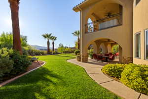 View of grassy yard with a patio, ceiling fan, a balcony, and a mountain view