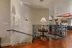 Stairway with ceiling fan, a raised ceiling, wood finished floors, recessed lighting, and arched walkways