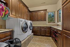 Laundry room with cabinet space, washing machine and dryer, and light stone finish floors