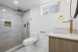 Full bath with vanity, tiled shower, and light tile patterned flooring