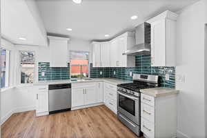 Kitchen with stainless steel appliances, white cabinets, decorative backsplash, light wood-type flooring, and recessed lighting
