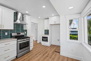 Kitchen featuring stainless steel gas range oven, white cabinetry, light wood finished floors, light stone countertops, and recessed lighting
