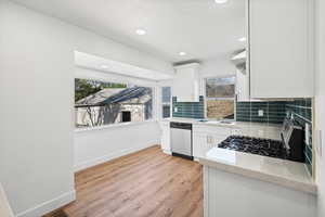 Kitchen featuring decorative backsplash, light wood finished floors, light stone countertops, stainless steel appliances, and white cabinets
