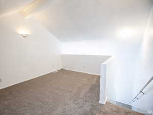 Additional living space with dark colored carpet and beamed ceiling