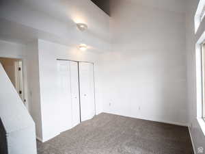 Unfurnished bedroom with dark carpet, a closet, and a high ceiling