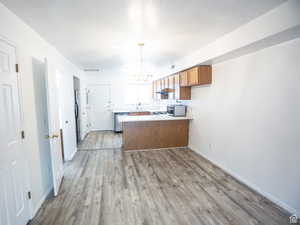 Kitchen with light countertops, a chandelier, wood finish cabinets, a peninsula, and dark wood finished floors