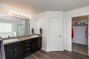 Full bathroom featuring a spacious closet, double vanity, a bath, a stall shower, and dark wood finished floors
