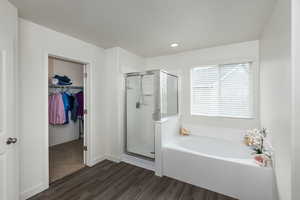 Full bathroom with a walk in closet, dark wood-style flooring, a stall shower, a bath, and recessed lighting