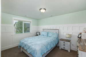Bedroom featuring a decorative wall, a wainscoted wall, and dark carpet