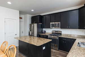Kitchen featuring dark cabinets, stainless steel appliances, light stone countertops, dark wood-style flooring, and recessed lighting
