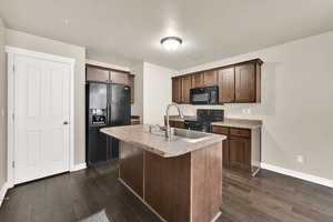 Kitchen with black appliances, a kitchen island with sink, dark wood finished floors, dark wood finish cabinetry, and a textured ceiling