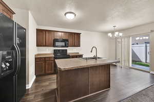 Kitchen featuring black appliances, an island with sink, dark wood-style flooring, a textured ceiling, and dark wood finish cabinetry