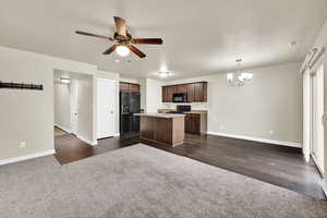 Kitchen with black appliances, a ceiling fan, dark colored carpet, suspended lighting, and a center island with sink