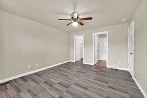 Unfurnished bedroom featuring a walk in closet, dark carpet, ceiling fan, and ensuite bathroom