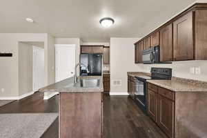 Kitchen featuring black appliances, light countertops, dark wood finished floors, a center island with sink, and dark wood finish cabinets