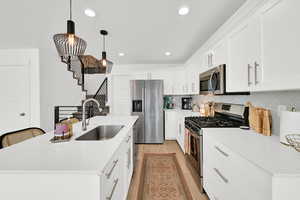 Kitchen with stainless steel appliances, a kitchen island with sink, white cabinetry, and light stone countertops