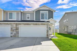 View of front of property featuring stone siding, board and batten siding, an attached garage, a front lawn, and driveway
