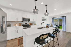 Kitchen with stainless steel appliances, white cabinets, wood tiled floors, an island with sink, and light stone counters