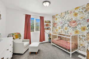 Bedroom featuring a crib, wallpapered walls, carpet, and an accent wall