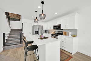 Kitchen with white cabinets, a breakfast bar, stainless steel appliances, wood finish floors, and a center island with sink
