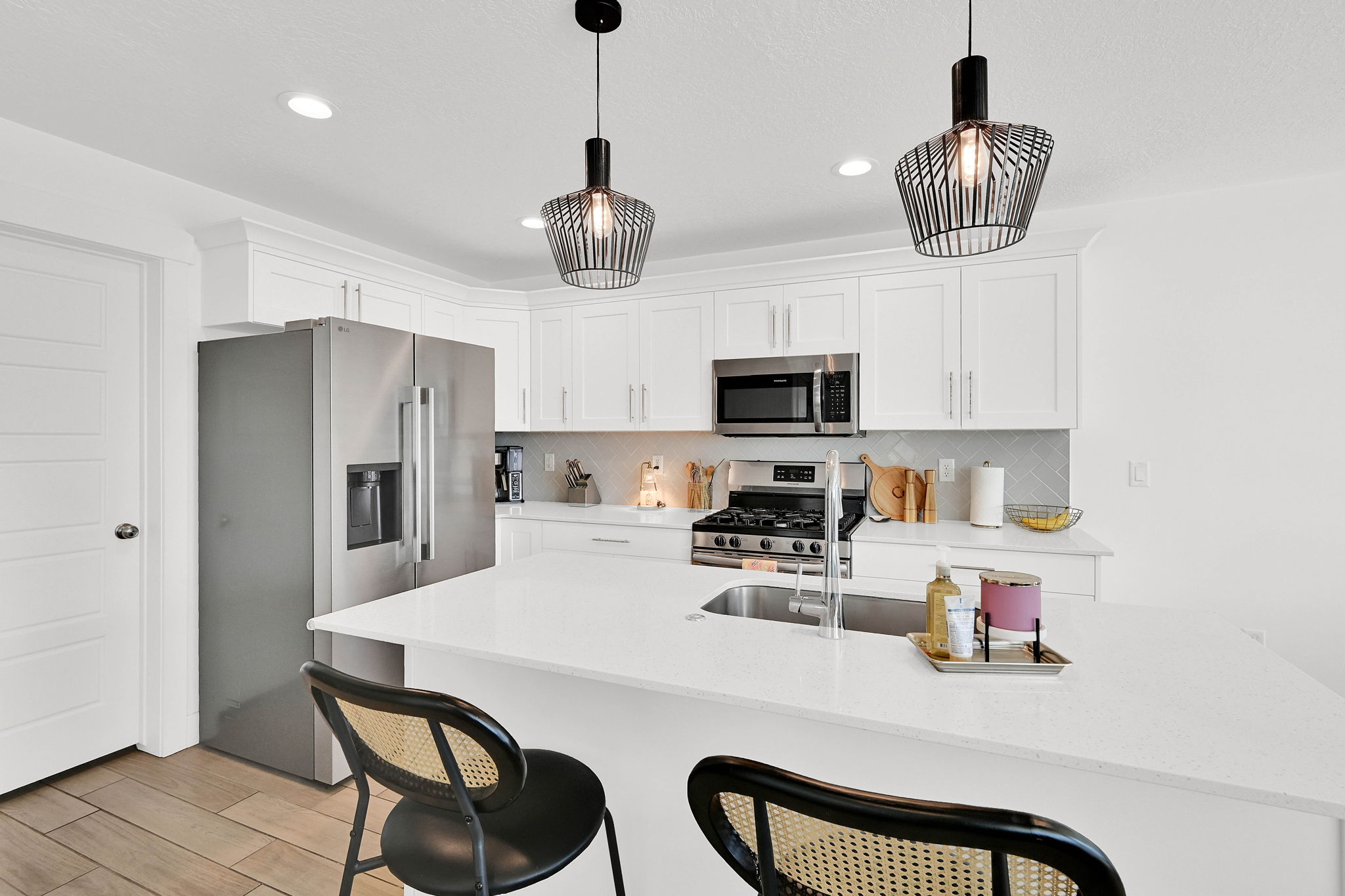 Kitchen with a breakfast bar, stainless steel appliances, white cabinetry, light stone countertops, and an island with sink