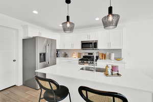 Kitchen with a breakfast bar, stainless steel appliances, white cabinetry, light stone countertops, and an island with sink
