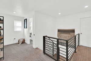 Hallway with light colored carpet, recessed lighting, and an upstairs landing