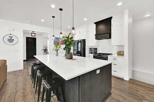 Two tone kitchen featuring a kitchen bar, a large island, two tone cabinetry, fridge with ice dispenser, and gas range