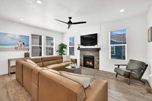 Living area featuring light wood finished floors, ceiling fan, a fireplace, recessed lighting, and plenty of natural light