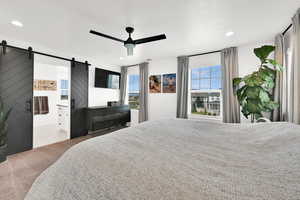 Carpeted bedroom with a barn door, a ceiling fan, connected bathroom, and recessed lighting