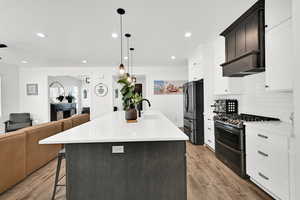 Kitchen featuring stainless steel appliances, open floor plan, a kitchen bar, a center island with sink, and light stone countertops