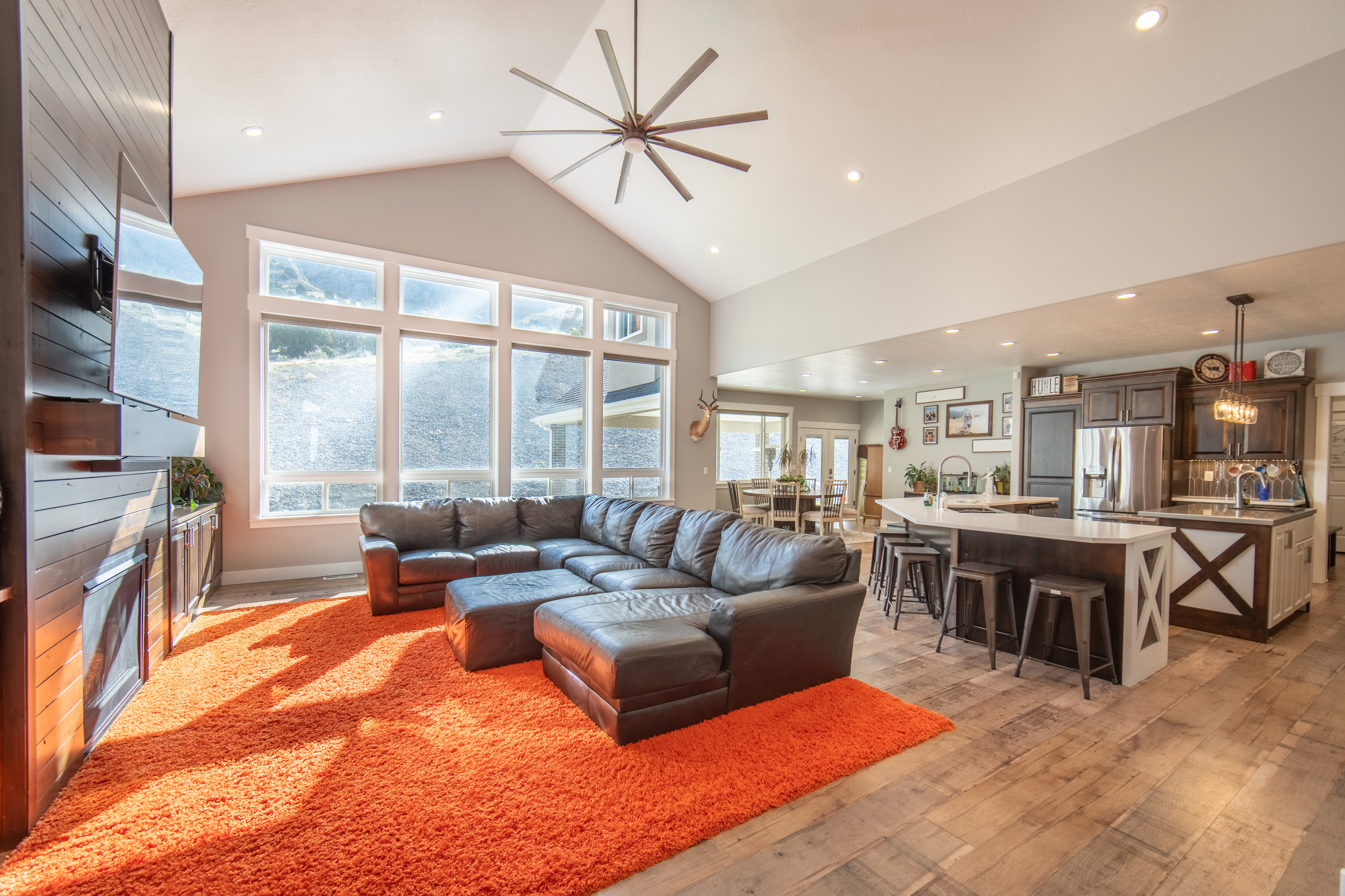 Living room featuring a ceiling fan, a fireplace, wood finished floors, recessed lighting, and a high ceiling